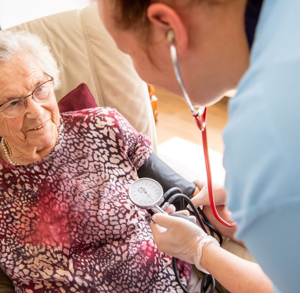 Pflegekraft von Ambulantem Pflegedienst am Greifpark Salzgitter misst Blutdruck einer älteren Frau zu Hause.