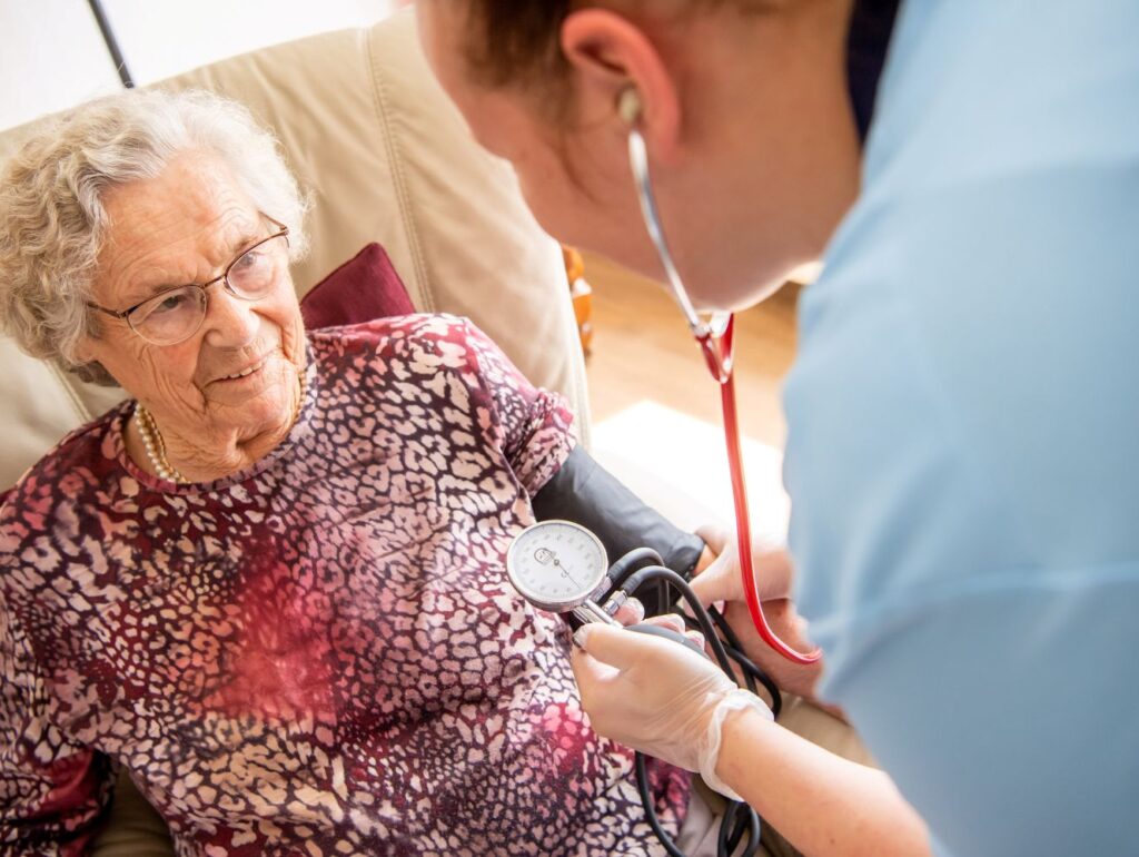 Pflegekraft von Ambulantem Pflegedienst am Greifpark Salzgitter misst Blutdruck einer älteren Frau zu Hause.