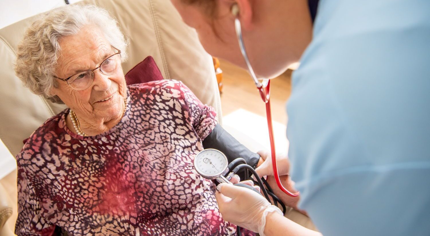 Pflegekraft von Ambulantem Pflegedienst am Greifpark Salzgitter misst Blutdruck einer älteren Frau zu Hause.