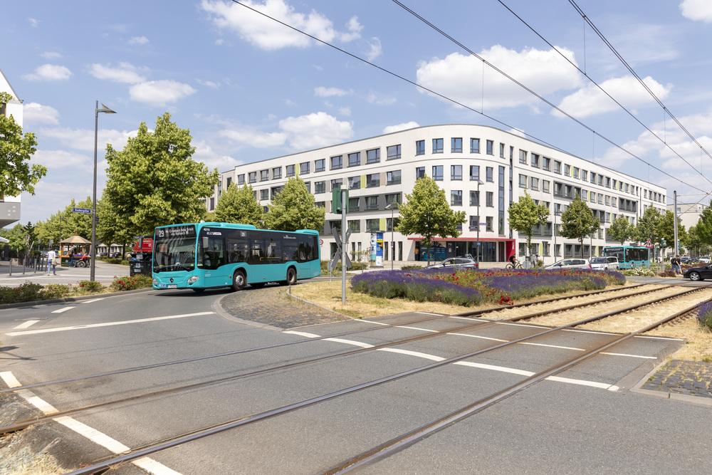 Korian Pflegeheim Haus der Betreuung und Pflege Bettinahof in Frankfurt von Außen gegenüber der Straße. Direkt gegenüber ist ein Rewe Supermarket und ein Apotheke sowie eine Straßenbahnhaltestelle