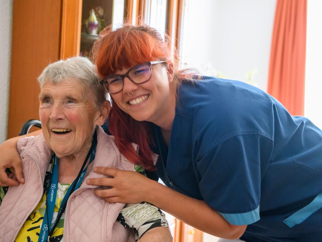 Weibliche Pflegekraft umarmt ältere Frau im Rollstuhl bei der häuslichen Betreuung durch den ambulanten Korian Pflegedienst Pflege und Betreuung zuhause am Jahnpark in Altenburg.