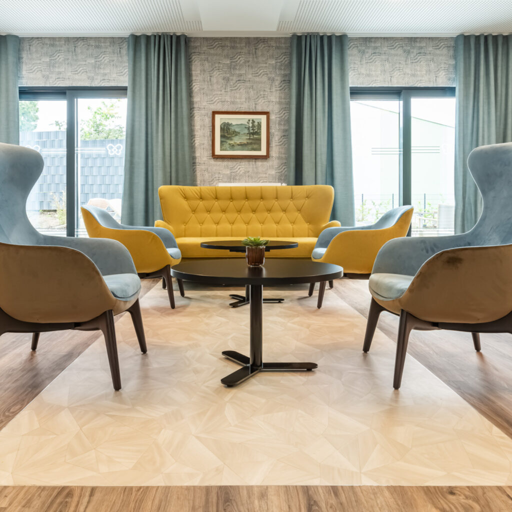 Bewohner:innen des Pflegeheims am Carree sitzen im hellen Gemeinschaftsraum in Riegelsberg und trinken gemeinsam Kaffee.