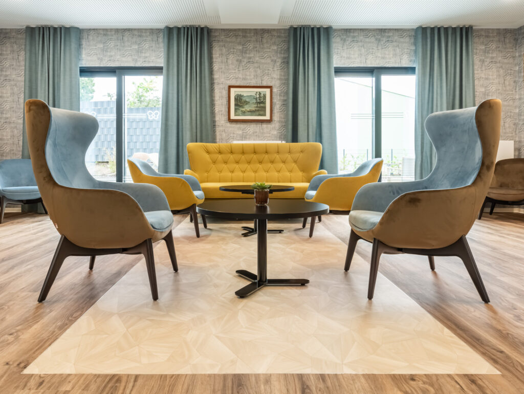 Bewohner:innen des Pflegeheims am Carree sitzen im hellen Gemeinschaftsraum in Riegelsberg und trinken gemeinsam Kaffee.