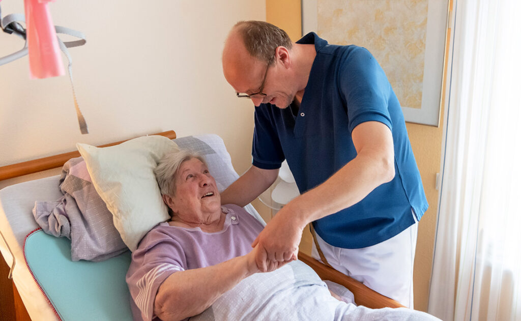 Pflegekraft hilft einer bettlägerigen älteren Frau im Bett, um Dekubitus vorzubeugen