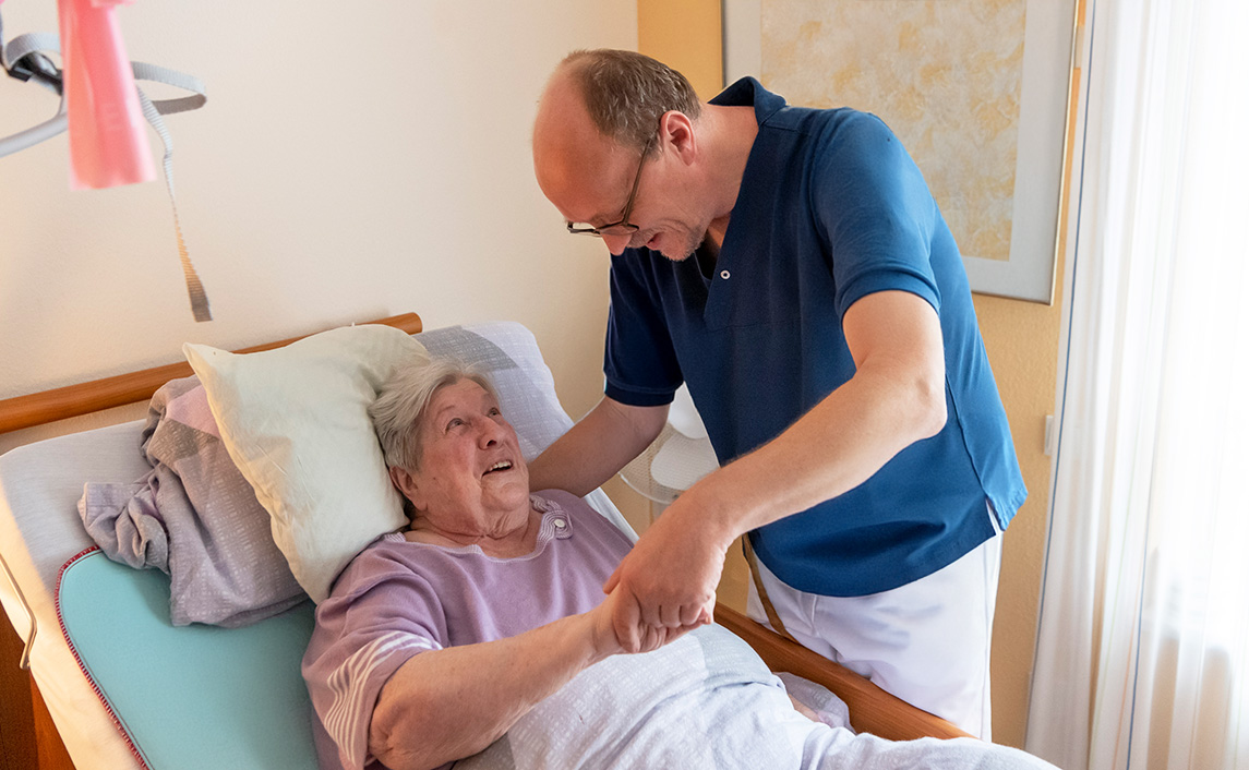 Pflegekraft hilft einer bettlägerigen älteren Frau im Bett, um Dekubitus vorzubeugen