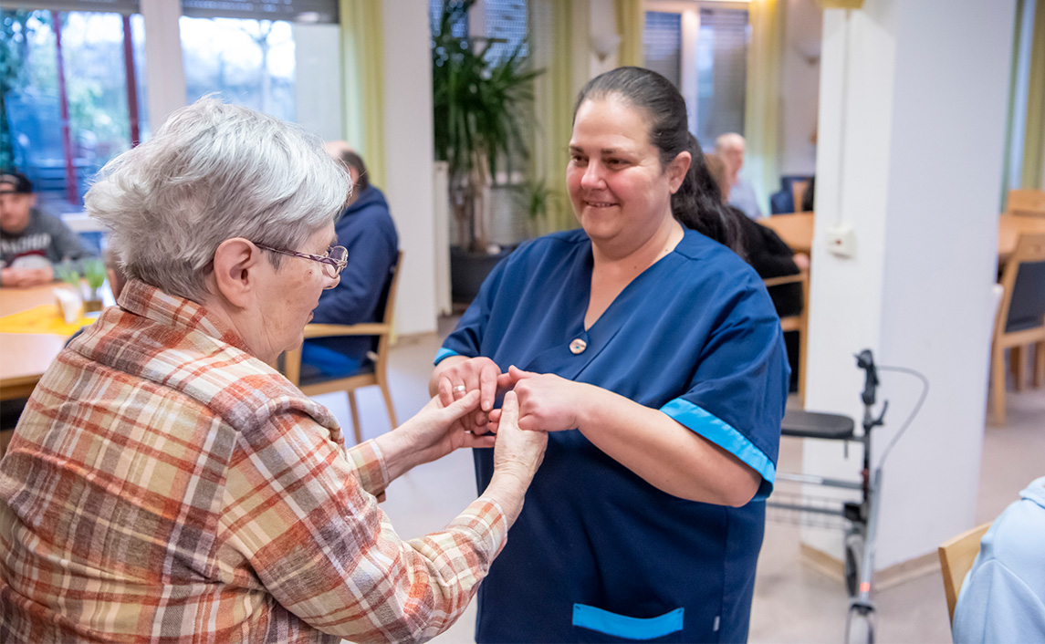 Pflegekraft hält die Hände einer Seniorin in einer Pflegeeinrichtung und lächelt einfühlsam - Pflegekompetenzgesetz stärkt Verantwortung in der Pflege