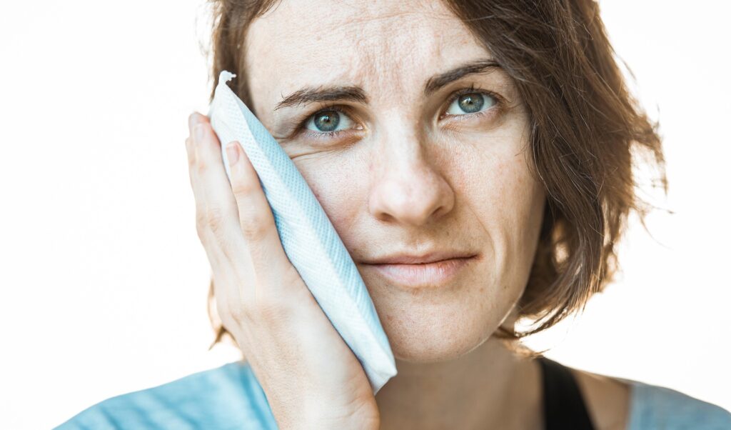 Eine junge Frau hat akute Zahnschmerzen und hält sich einen Eisbeutel gegen die Wange.