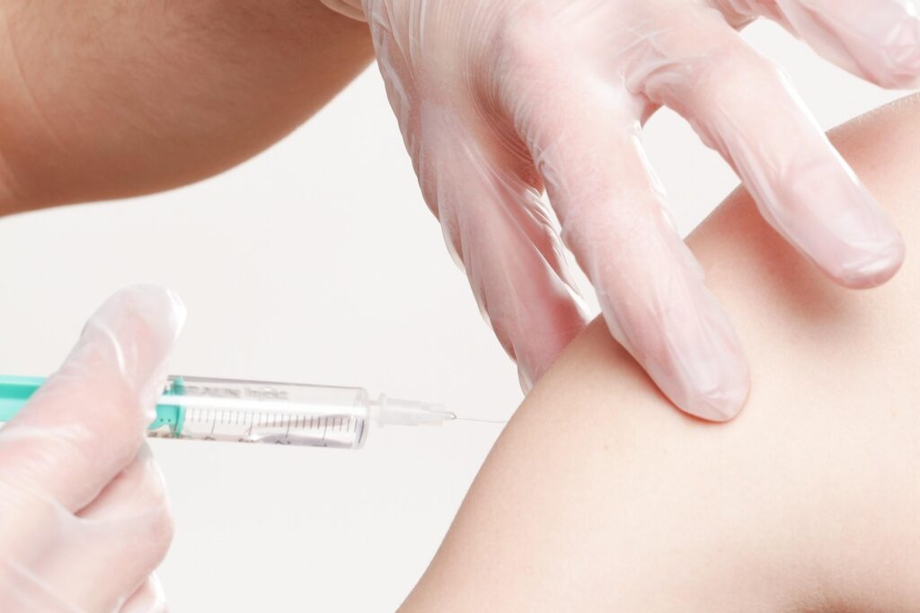 Jemand bekommt von jemandem, der Handschuhe trägt eine Spritze bzw. Gürtelrose-Impfung (oder Herpes zoster) in den Oberarm; Nahaufnahme.