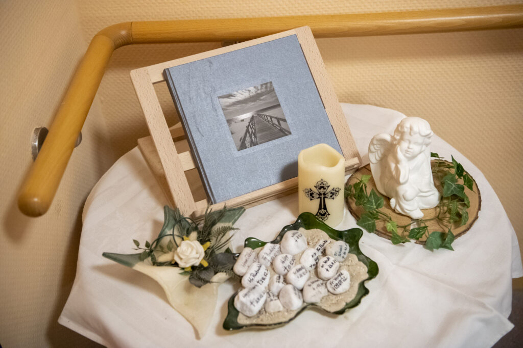 Korian Ratgeber Artikel; Tisch mit Kondolenzbuch, Kerze, Engel und Namen zum Abschied nehmen und Trauerbewältigung im Todesfall
