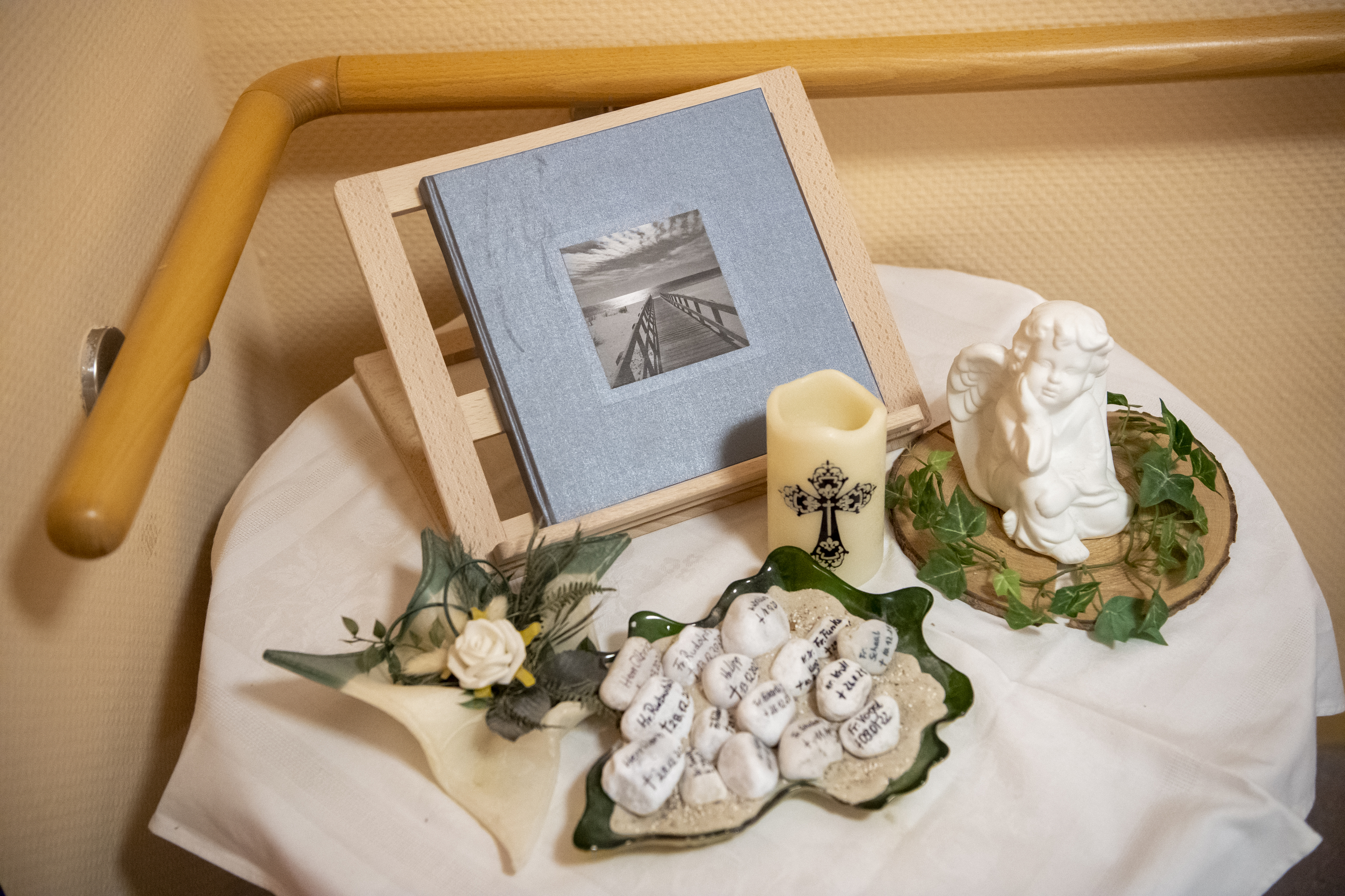 Korian Ratgeber Artikel; Tisch mit Kondolenzbuch, Kerze, Engel und Namen zum Abschied nehmen und Trauerbewältigung im Todesfall